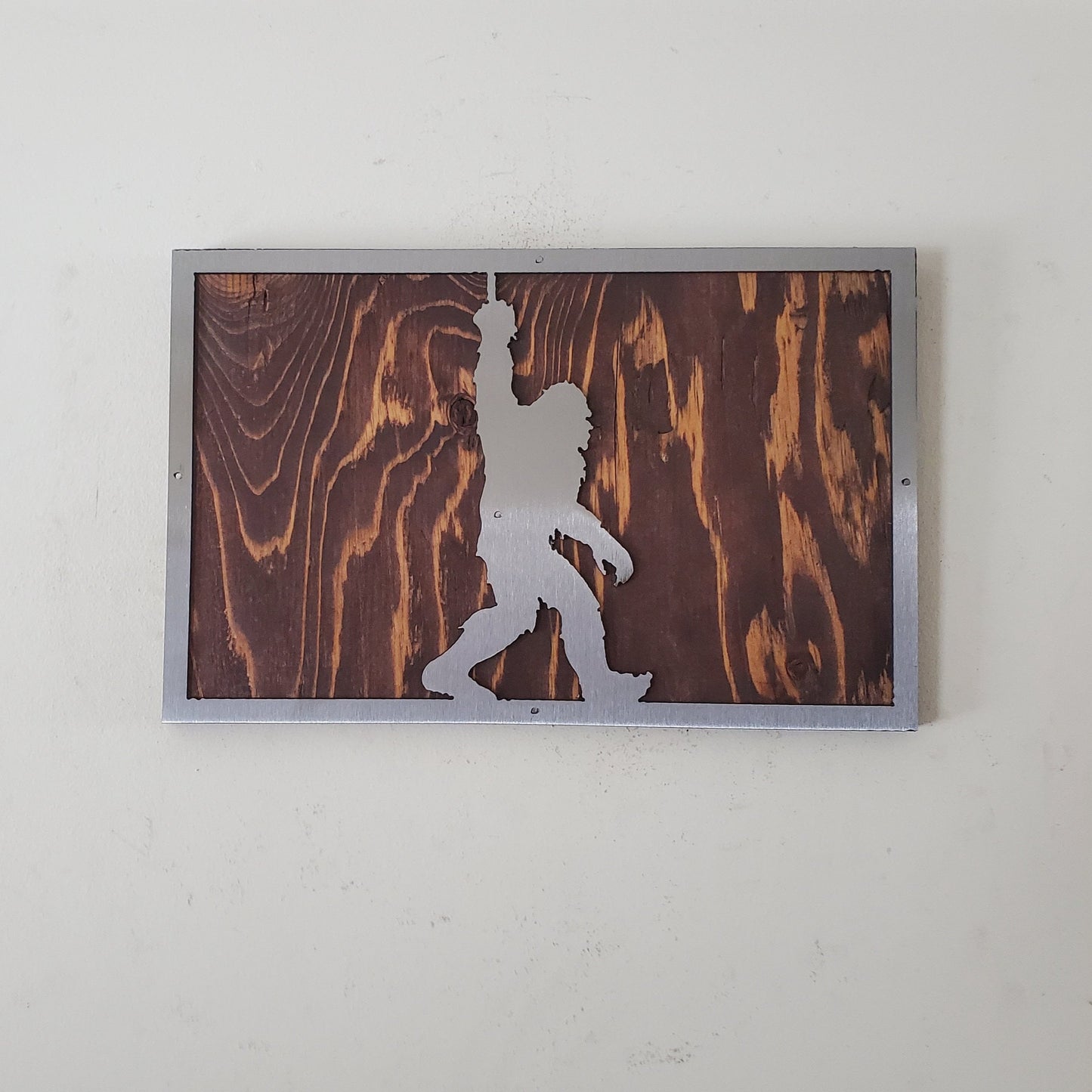 A unique metal art sculpture of bigfoot, mounted on a wooden background. The sculpture is made of high-quality metal and features a realistic design that captures the essence of the mythical creature.