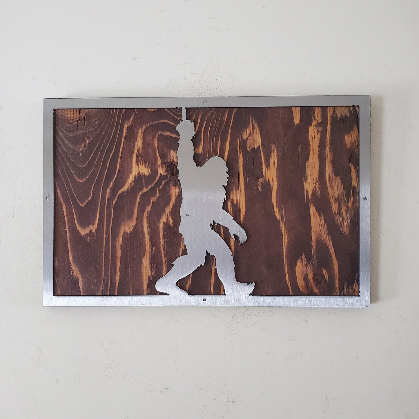 A unique metal art sculpture of bigfoot, mounted on a wooden background. The sculpture is made of high-quality metal and features a realistic design that captures the essence of the mythical creature.