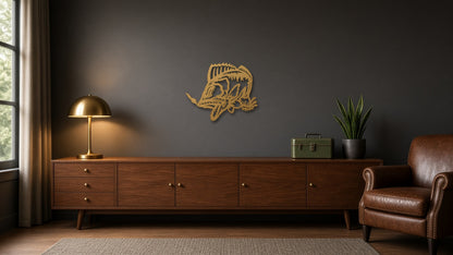 A styled interior scene with a dark wood sideboard against a charcoal wall, a brass table lamp on the left, a small green box and potted plant in the center-right, and a brown leather armchair on the right. A gold-toned decorative wall piece hangs above the sideboard.