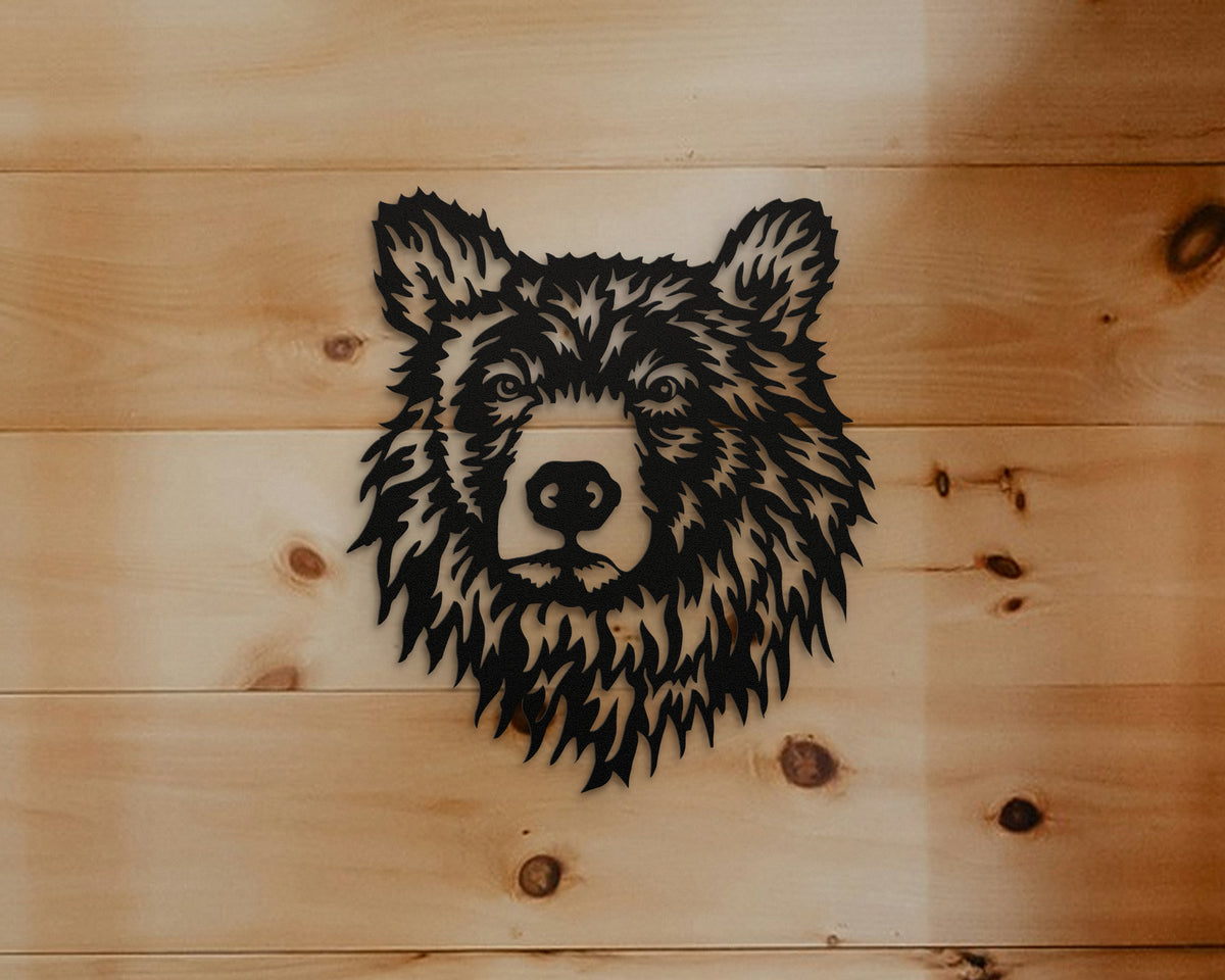 A black metal wall art piece shaped like a bear head, mounted on a light natural wood plank wall.
