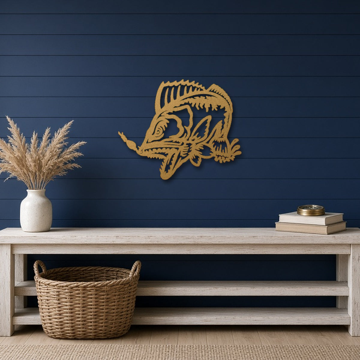 A gold metal fish wall art piece mounted on a dark navy blue shiplap wall above a light wood console table with a vase of dried grass and stacked books.