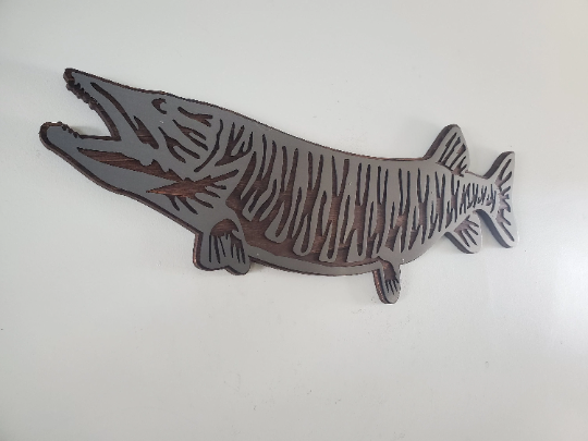 This Muskie fish sculpture art is a beautiful and unique wall decor piece, featuring an artistic representation of the elusive and challenging king catch - the Muskie. It is made using rustic stained wood and clear-coated steel