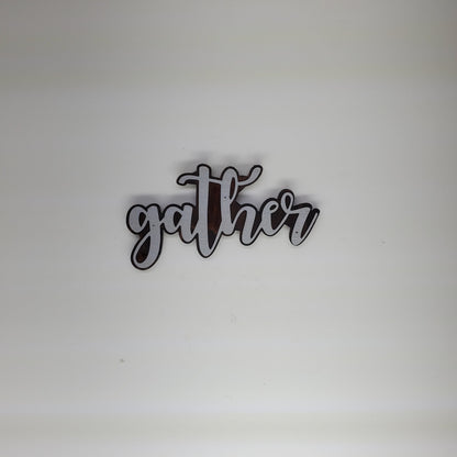 The metal art is cutout in the shape of the word "Gather", adding a touch of elegance and warmth to any room