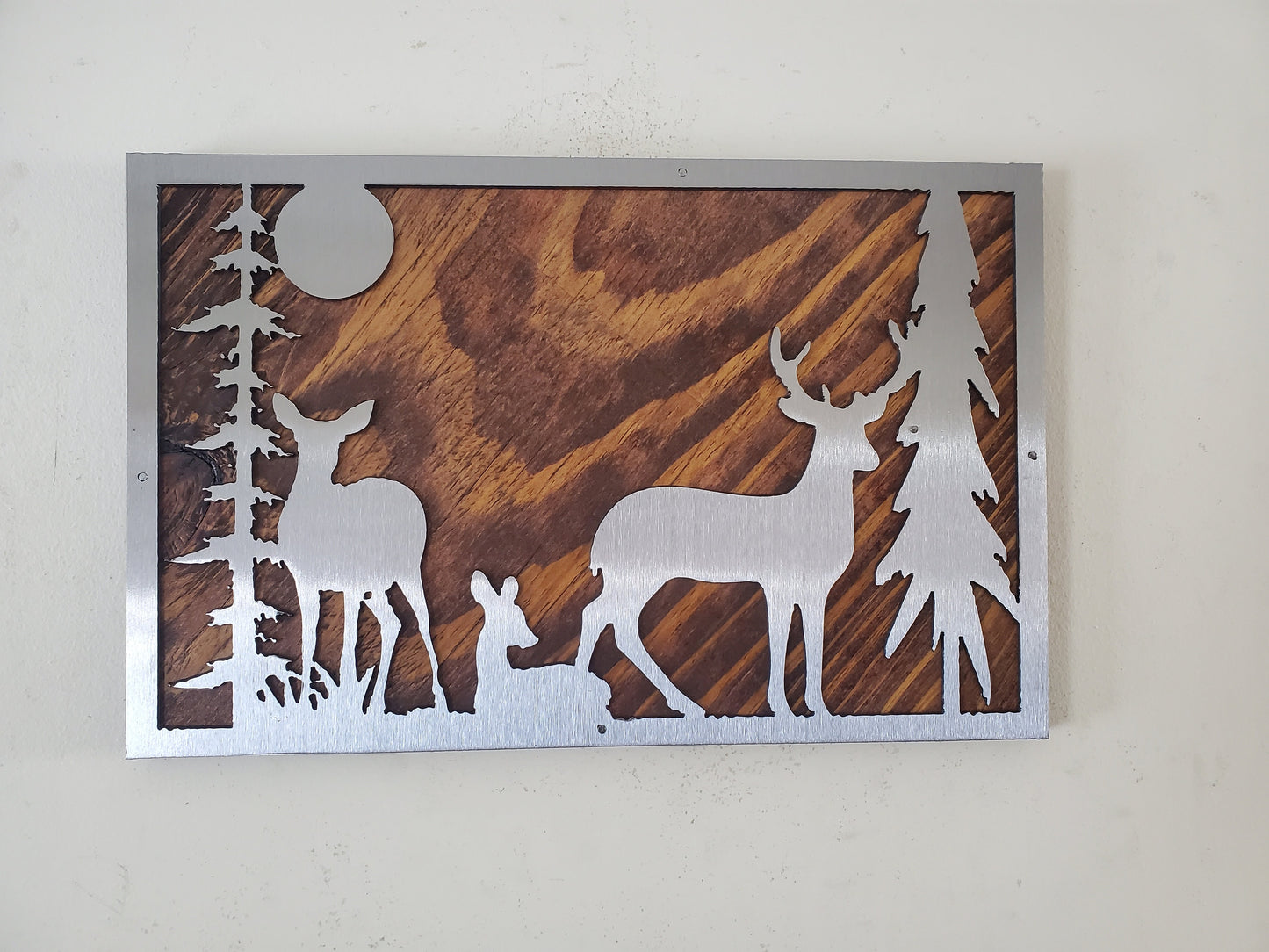 Metal art wall decor featuring a detailed and textured depiction of a deer in the woods, made of clear coated steel with rustic wood back.  A striking and unique piece, ideal for nature and outdoor enthusiasts.