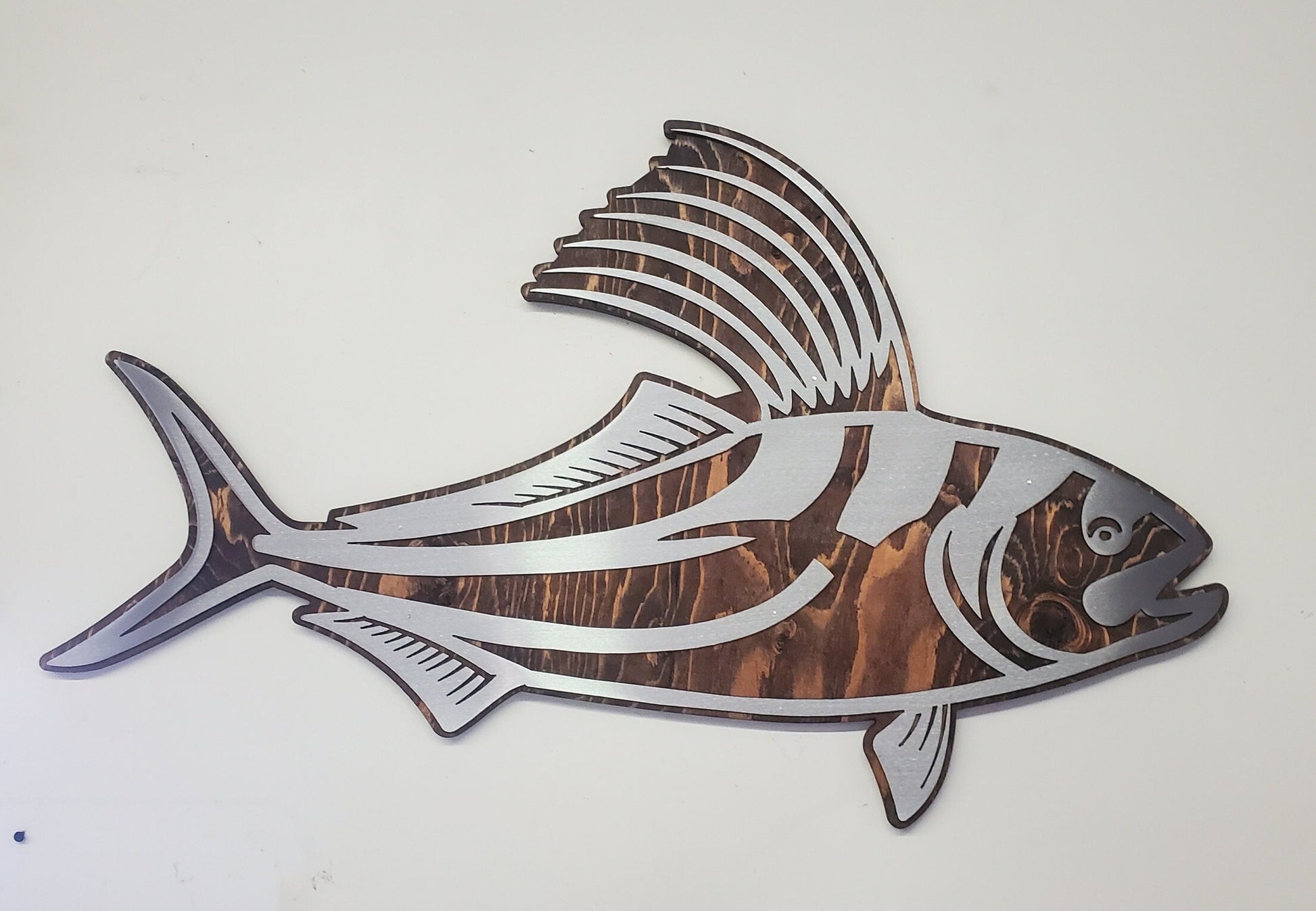 CNC cut metal rooster fish on a rustic stained wood background, handcrafted by a small family shop in Minnesota. The clear-coated steel rooster fish has intricate details and is designed for indoor or covered outdoor display