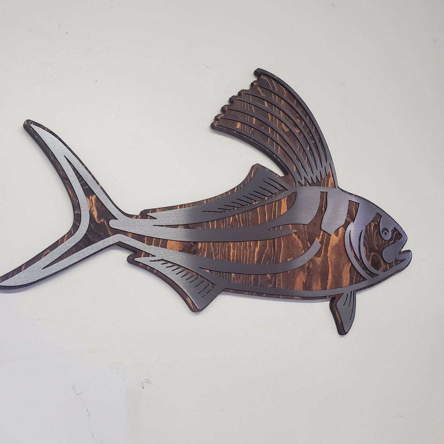 CNC cut metal rooster fish on a rustic stained wood background, handcrafted by a small family shop in Minnesota. The clear-coated steel rooster fish has intricate details and is designed for indoor or covered outdoor display