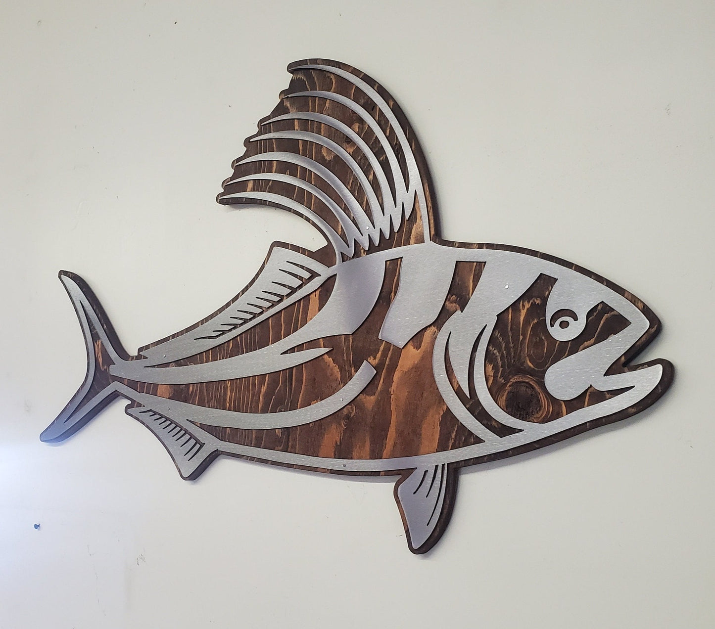 CNC cut metal rooster fish on a rustic stained wood background, handcrafted by a small family shop in Minnesota. The clear-coated steel rooster fish has intricate details and is designed for indoor or covered outdoor display